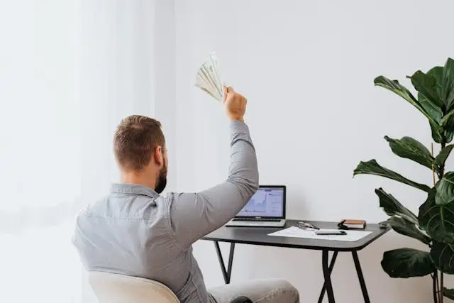 un hombre frente a u a laptop con dolares en la mano