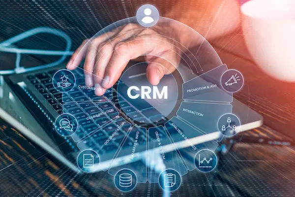 Mano escribiendo en un teclado con un icono de CRM y gráficos digitales, aplicando estrategias digitales.