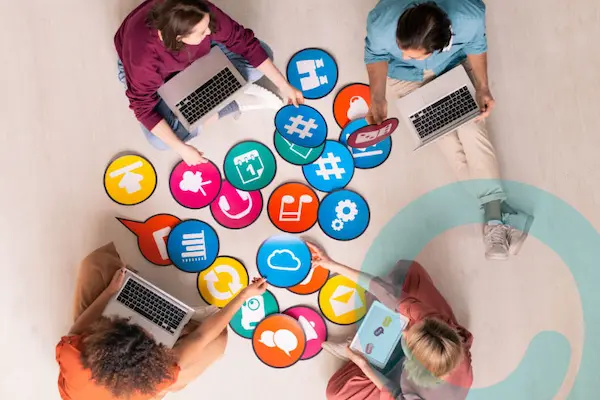 Personas con computadoras rodeadas de íconos digitales de redes sociales y tecnología, aplicando estrategias digitales.