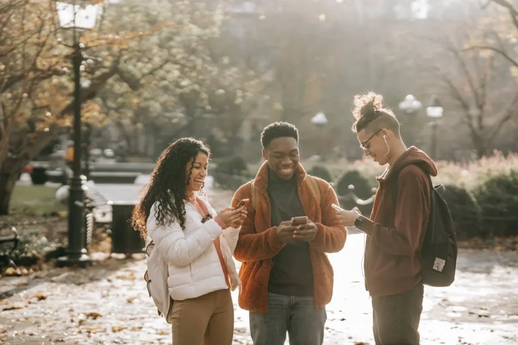 Grupo de jóvenes disfrutando de la tecnología móvil en un parque, destacando el impacto de la conectividad 5G en las actividades cotidianas y la comunicación instantánea.