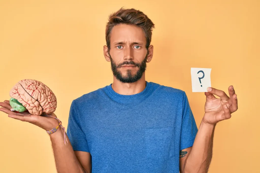 Hombre sosteniendo un cerebro y un signo de interrogación representando sesgos cognitivos