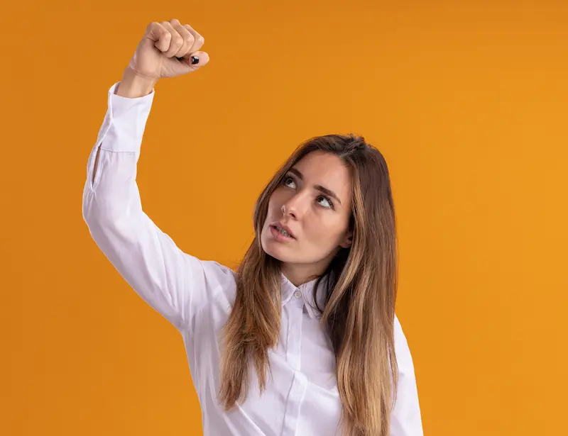 Mujer levantando el puño y mirando hacia arriba sobre fondo naranja