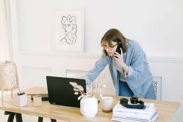 mujer con celular y frente a la laptop